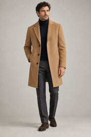 Male model wearing tailored overcoat in camel on a neutral studio background